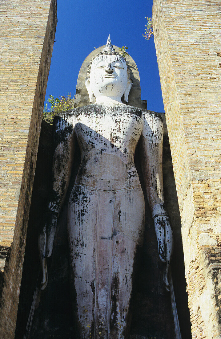 Thailand, Sukhotha, Tiefblick auf stehende Steinstatue zwischen Säulen; Wat Mahathat
