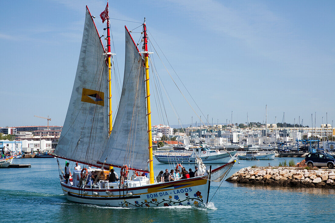 A Boat With Large Sails Travels Through The Harbour; Lagos Algarve Portugal