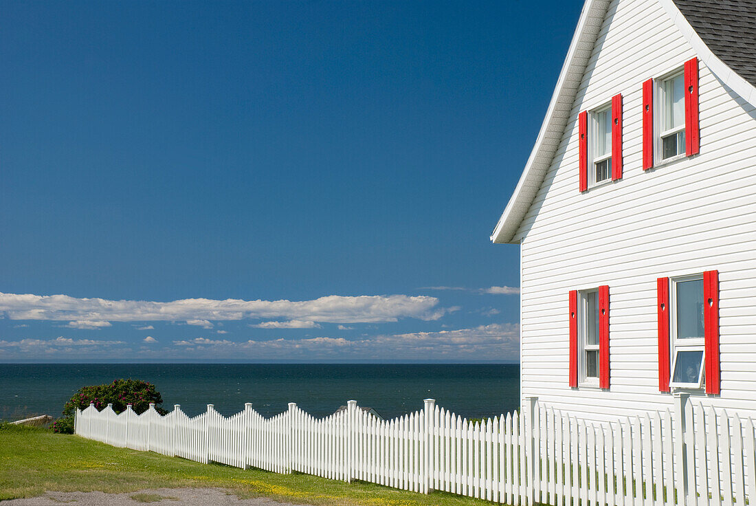 White House With Red Trim And A White Picket Fence By The Ocean; Gaspesie Quebec Canada