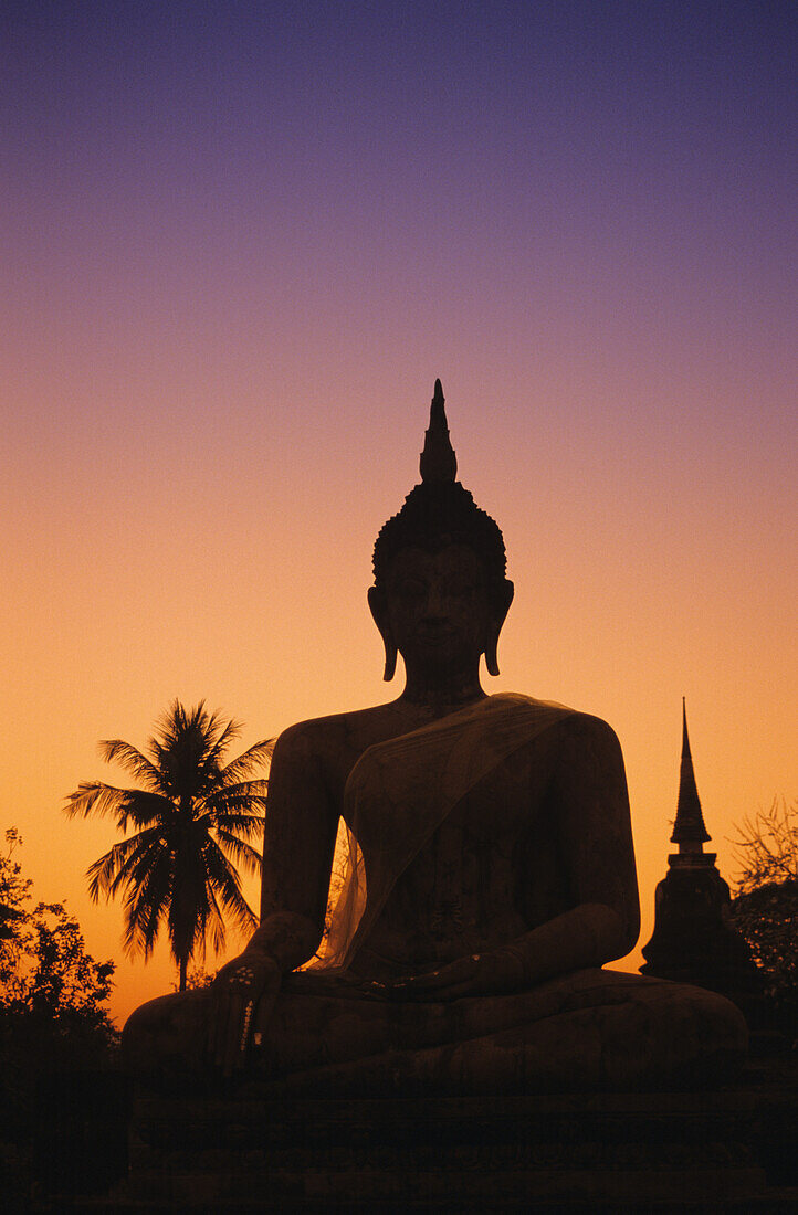 Thailand, Sukhothai, Wat Mahathat bei Sonnenuntergang, Buddha-Statue mit Scherenschnitt, lila und oranger Himmel.