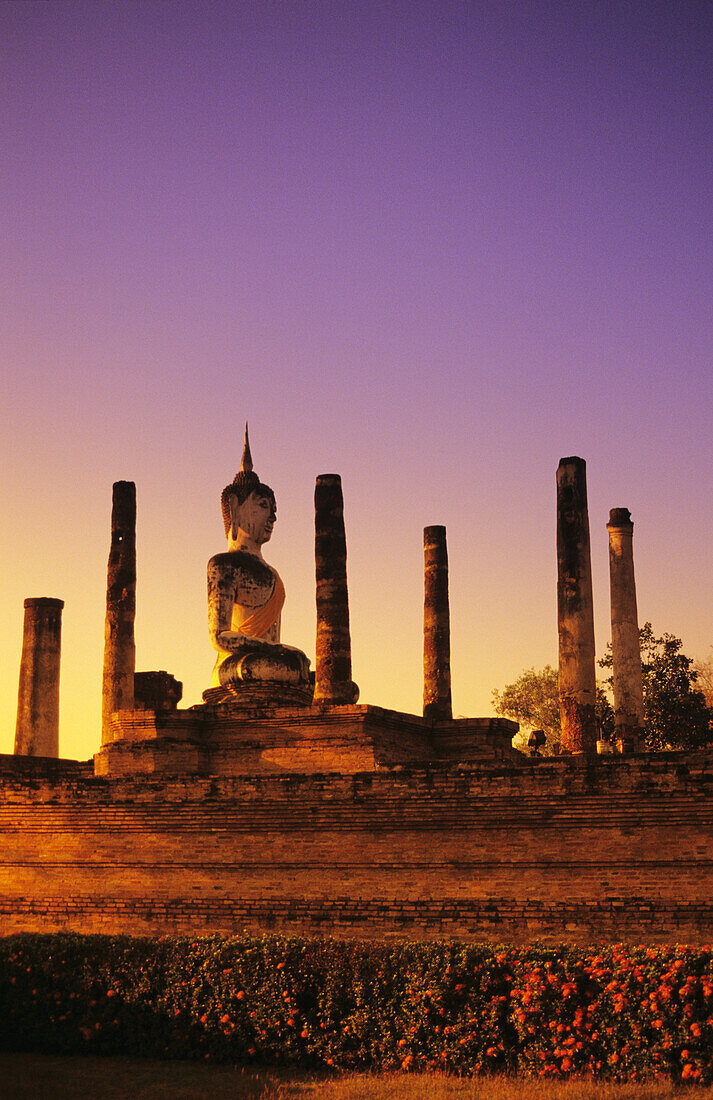 Thailand, Sukhothai, Glowing sunlight on structure of Buddha statue with many pillars at sunset; Wat Mahathat