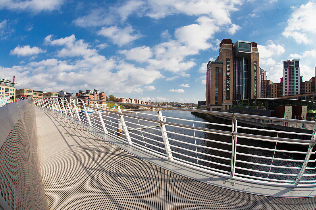 A Pedestrian Bridge Across River Tyne With Buildings Along The Waterfront; Newcastle Northumberland England