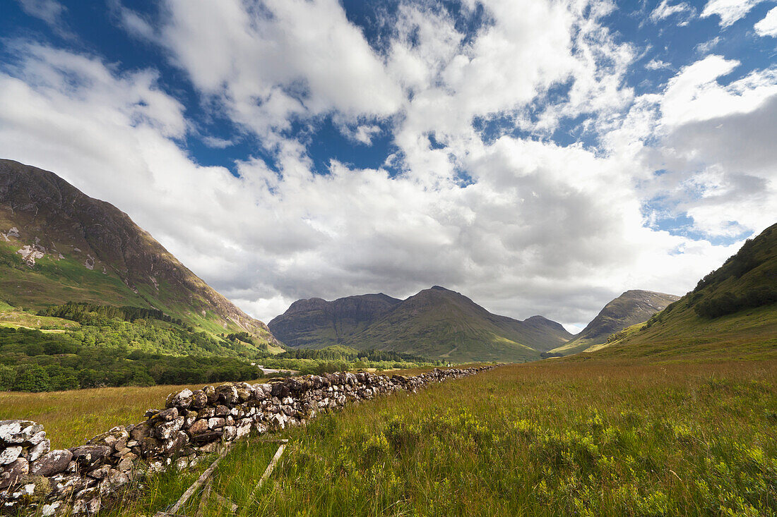 Eine Steinmauer durch die Felder mit Bergen in der Ferne; Glencoe Argyll Schottland