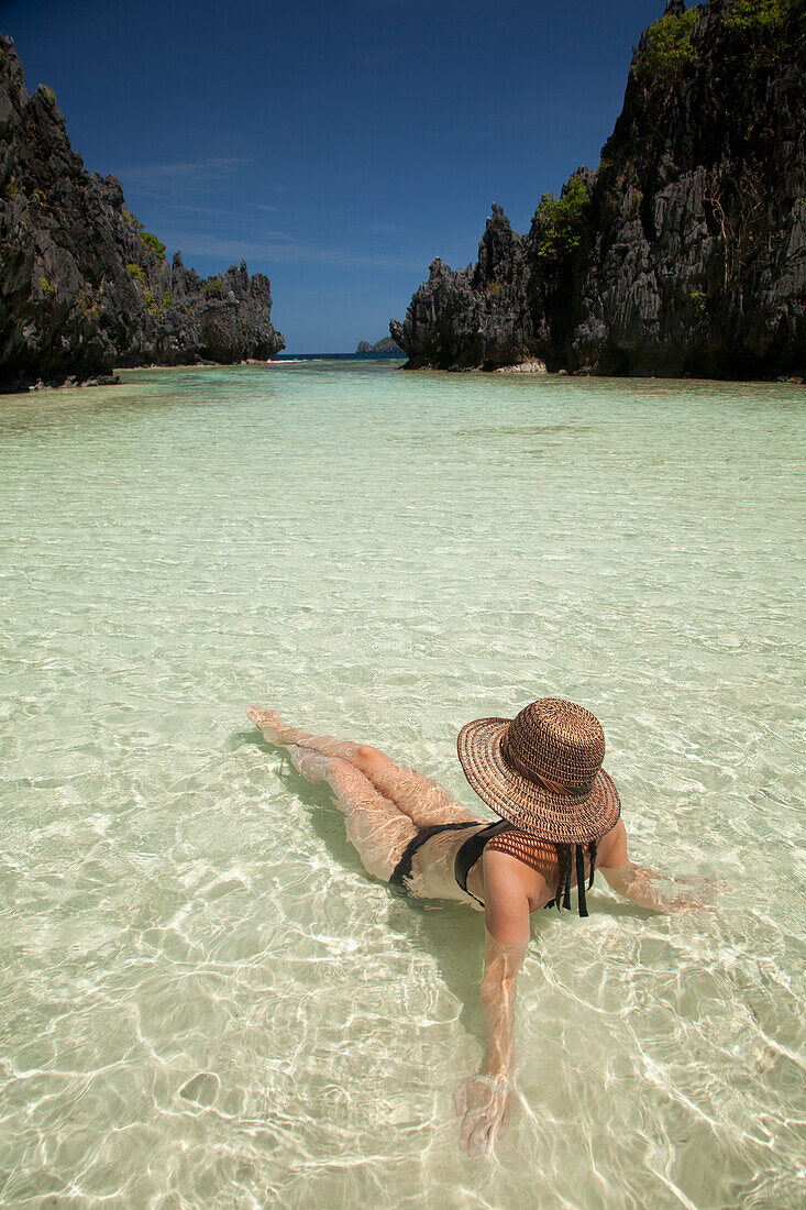 Eine Touristin mit Sonnenhut und Bikini entspannt sich im klaren Wasser der Insel Matinloc bei El Nido und Corong Corong; Bacuit Archipel Palawan Philippinen