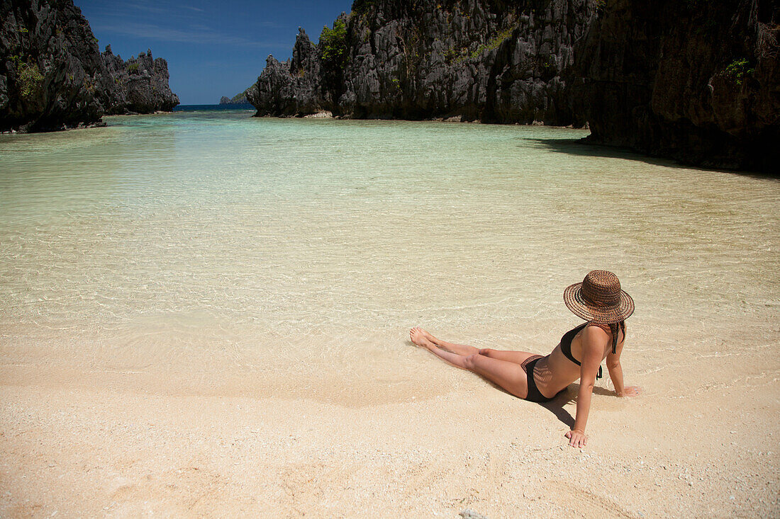 Eine Touristin mit Sonnenhut und Bikini entspannt sich im klaren Wasser der Insel Matinloc in der Nähe von El Nido und Corong Corong; Bacuit Archipelago Palawan Philippinen