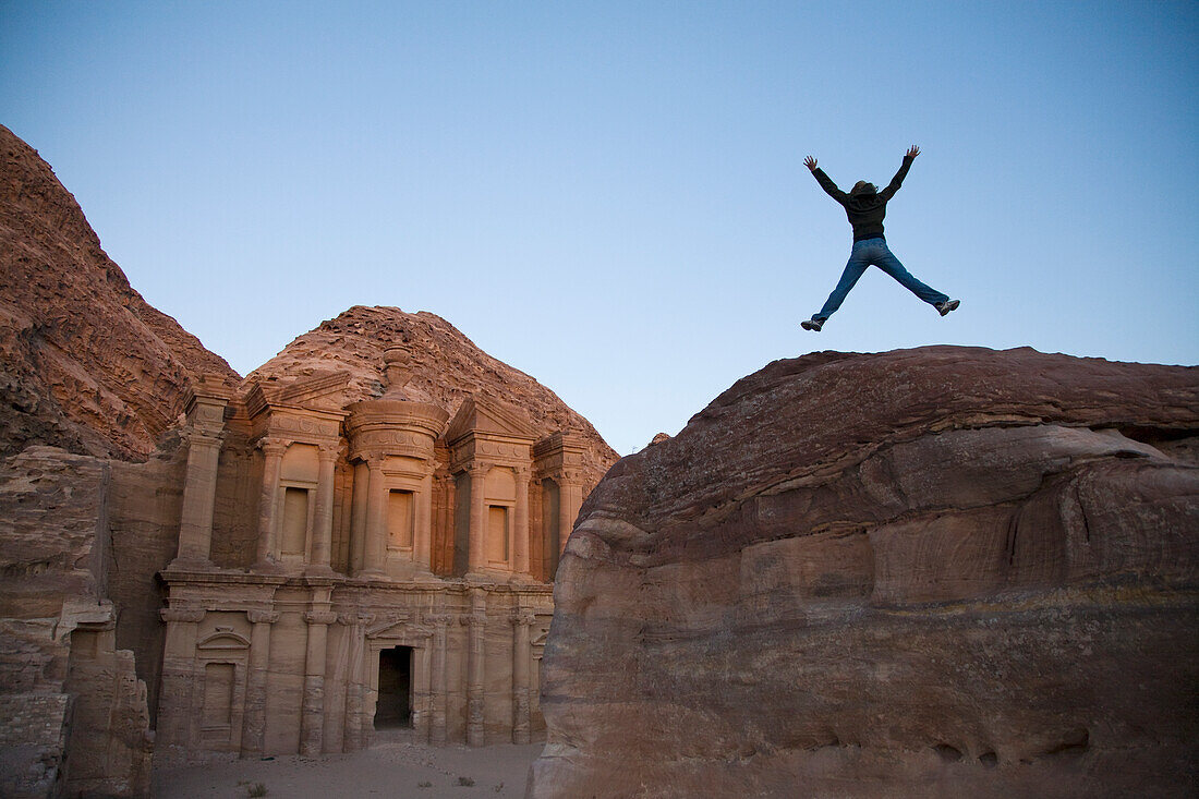 A Woman Tourist Jumps Into The Air In Front Of The Nabatean Ruins Of The Monastery; Petra Jordan