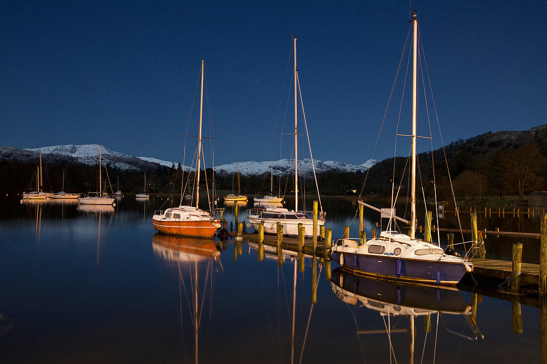 Schnee auf den Gipfeln der Berge, die sich im Wasser spiegeln, mit Booten, die im Windermere-See vertäut sind; Cumbria England