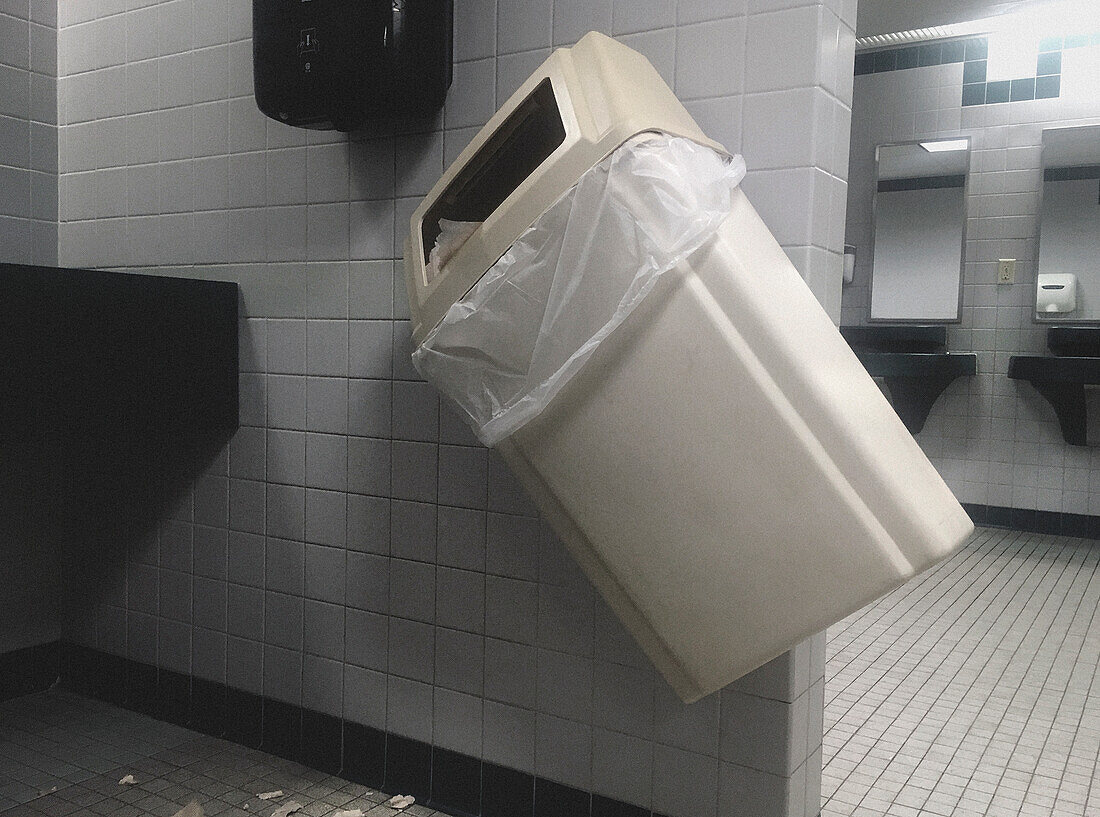Wall-Mounted Garbage Pail knocked on Angle in Public Bathroom
