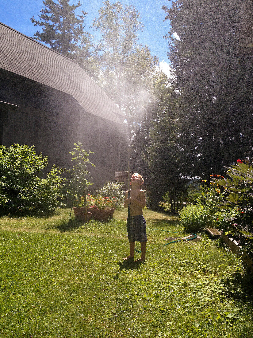 Junger Junge spielt mit Sprinklerschlauch im Garten