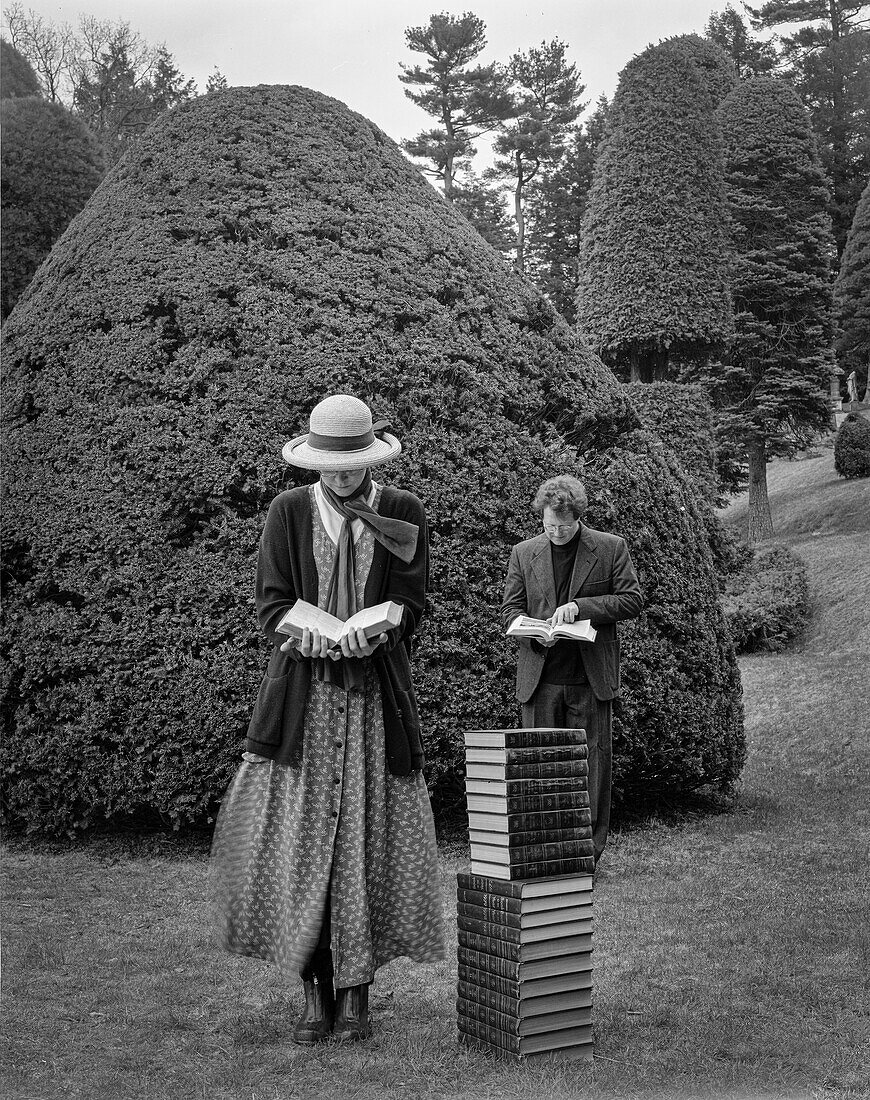 Mann und Frau stehen lesend neben einem Bücherstapel im Formschnittgarten
