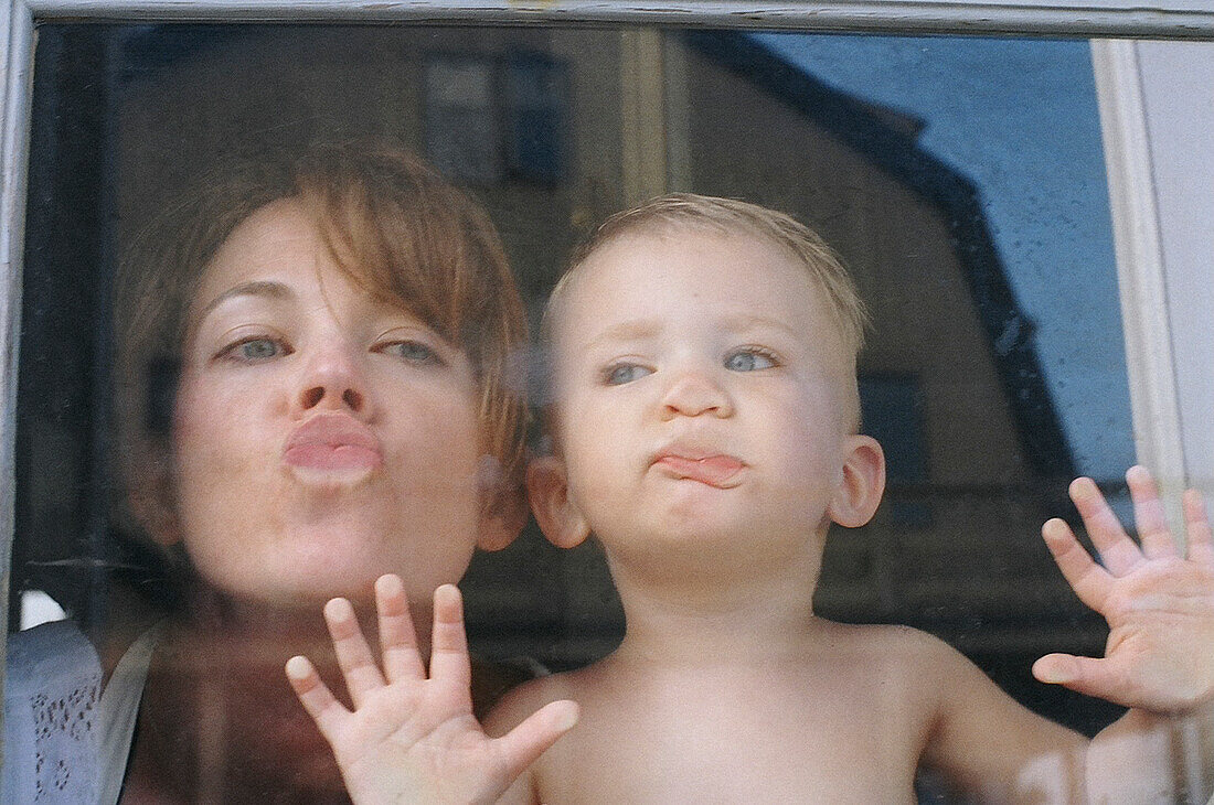 Mutter und junger Sohn drücken ihre Lippen unbeschwert gegen das Fenster