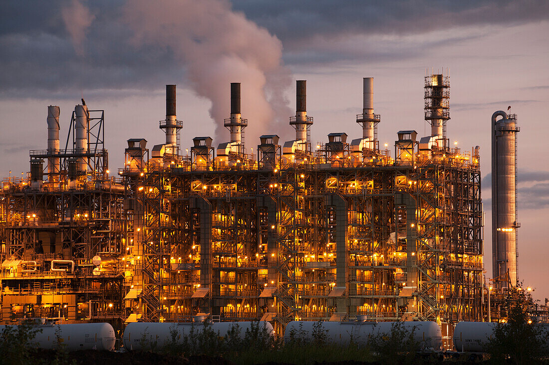 Towers Of A Refinery Illuminated By Lights At Dawn; Alberta Canada