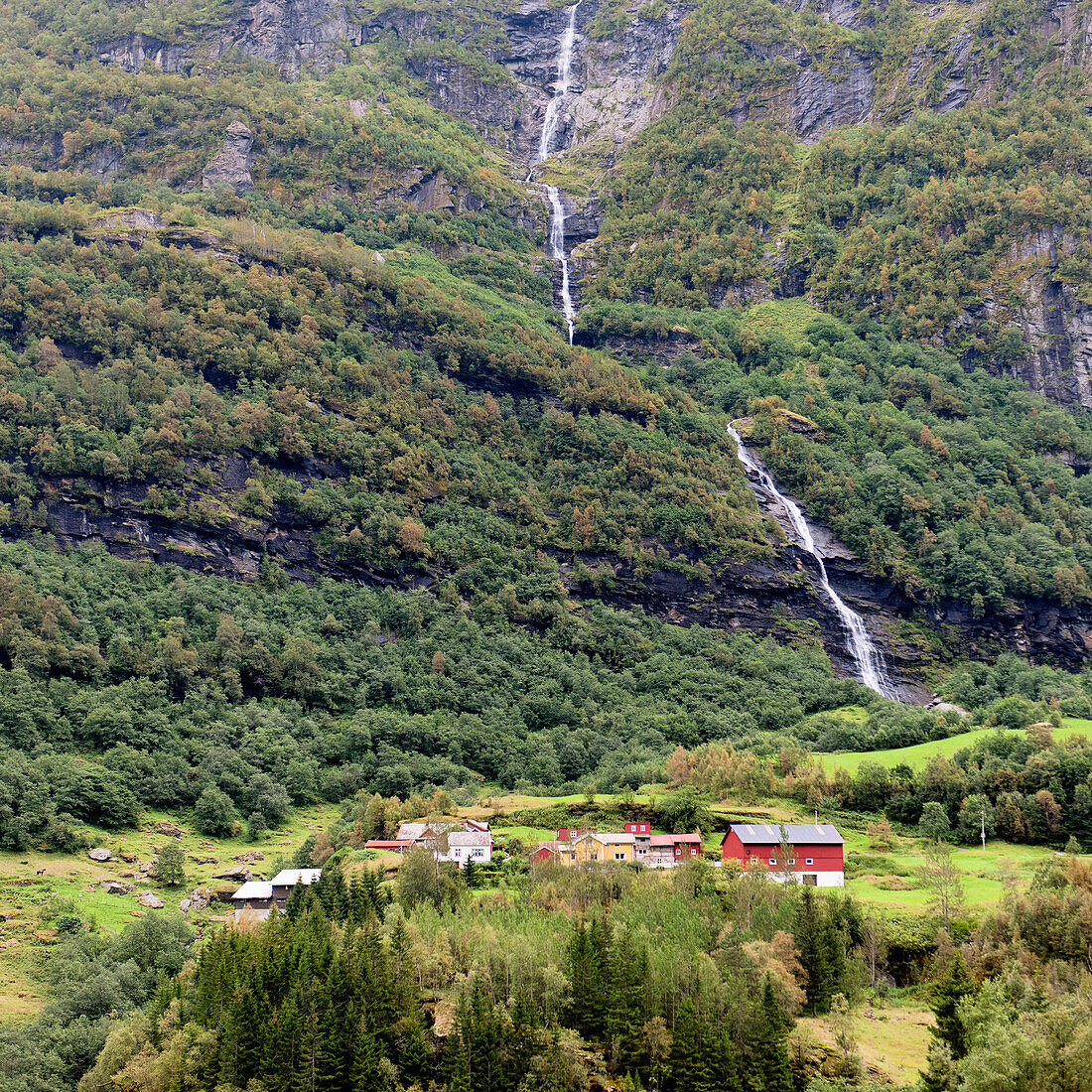 Ein Wasserfall an einem Berghang mit Häusern im Tal; Undredal Sognefjord Norwegen