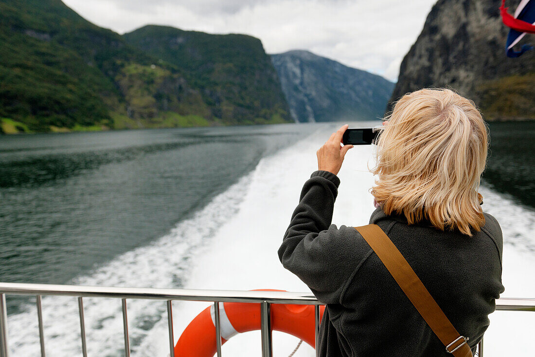 Eine Frau macht ein Foto mit ihrer Kamera vom Heck eines Bootes aus; Sognefjord Norwegen