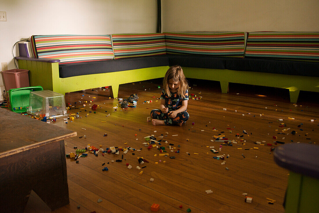 Junger Junge sitzt auf dem Boden eines großen Raumes, umgeben von Plastikspielzeugteilen