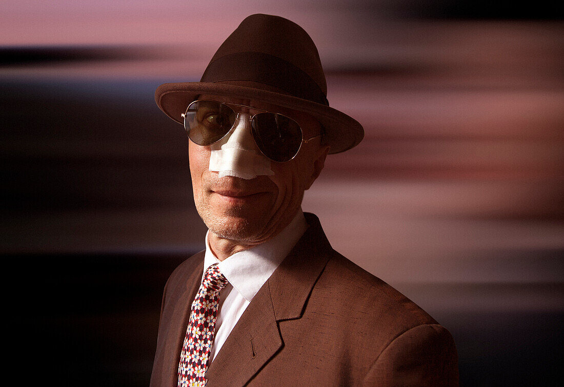 Man in suit, hat and sunglasses with bandage on his nose