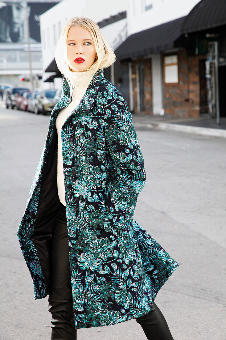 Young blonde woman in a white turtleneck sweater and transitional coat with leaf jacquard