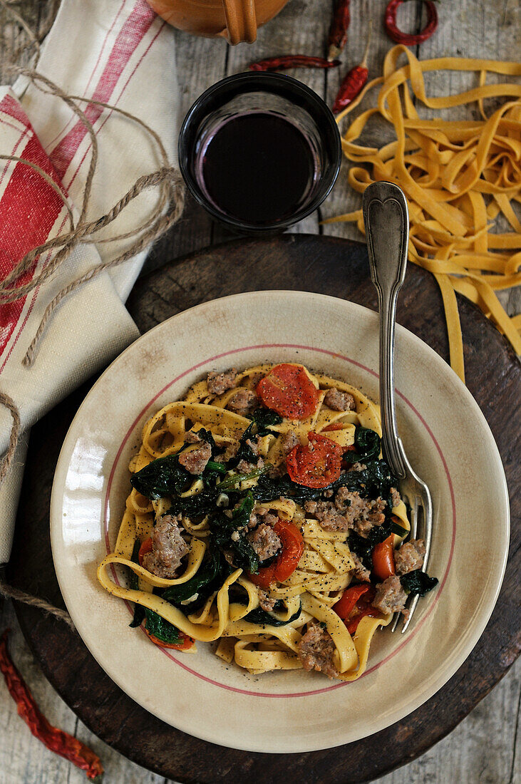 Homemade tagliatelle with sausage, spinach and tomatoes