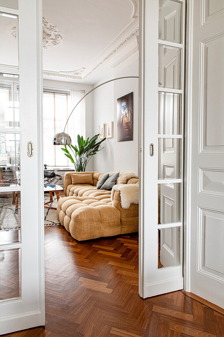 Blick durch geöffnete Glasschiebetüren ins Altbau-Wohnzimmer auf bequemes Sofa und Bogenlampe