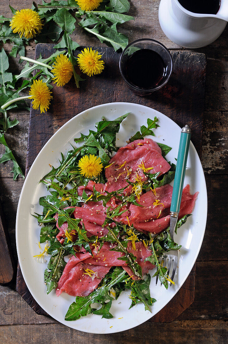 Beef carpaccio with dandelion leaves and dandelion flowers