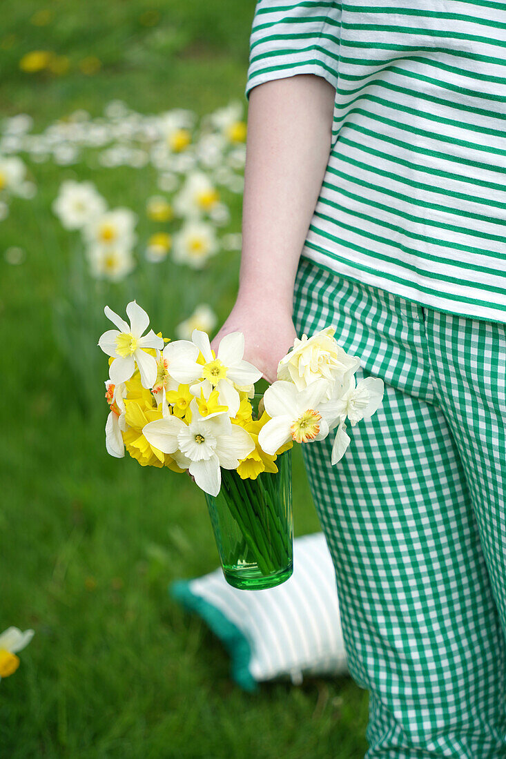 Person carrying glass with daffodils