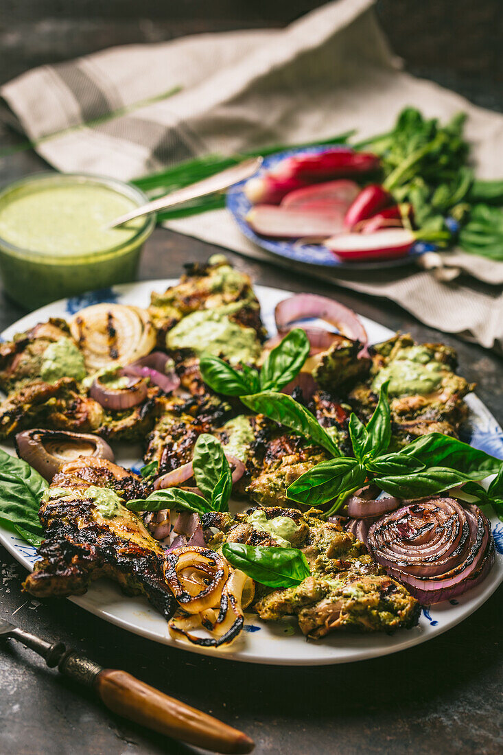 Gegrillte Hähnchenschenkel mit roten Zwiebeln und Basilikumblättern, dazu grüne Sauce