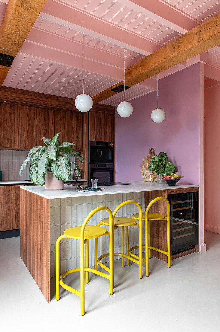 Kitchen corner with wooden elements and tiles, yellow stools and pink wall design