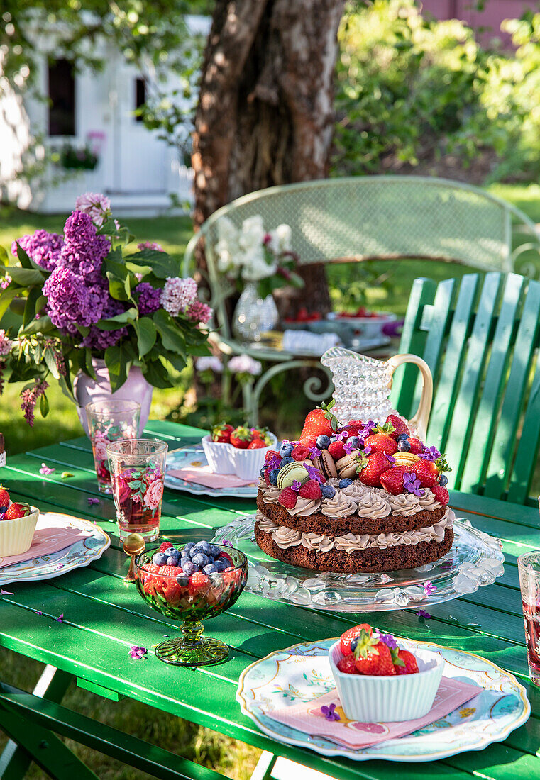 Garden table with chocolate cake and summer flowers in a vase