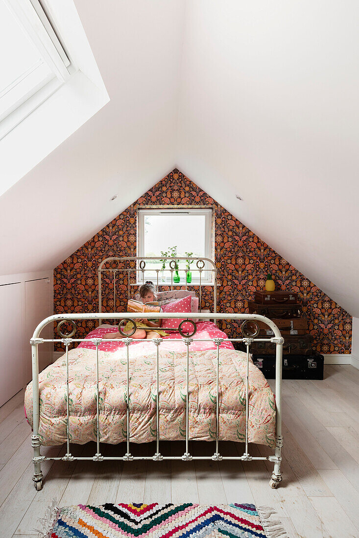 Girl sits riding on vintage metal framed bed in Guildford home, Surrey, UK