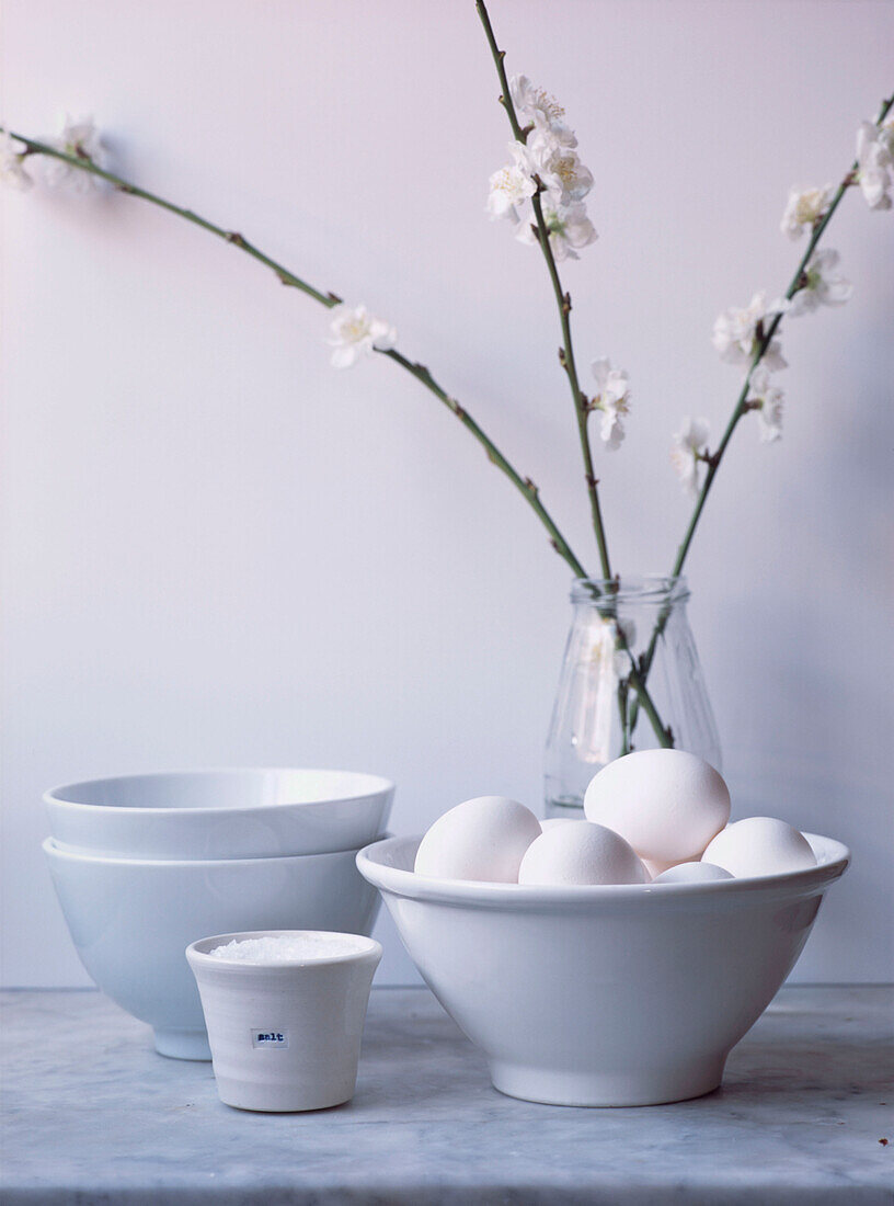 Still life in white of eggs in a bowl with apple blossom on a marble work top