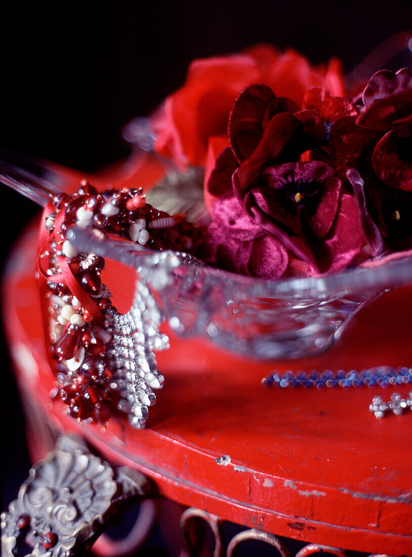 A glass bowl on a rustic dressing table containing silk flowers and jewellery