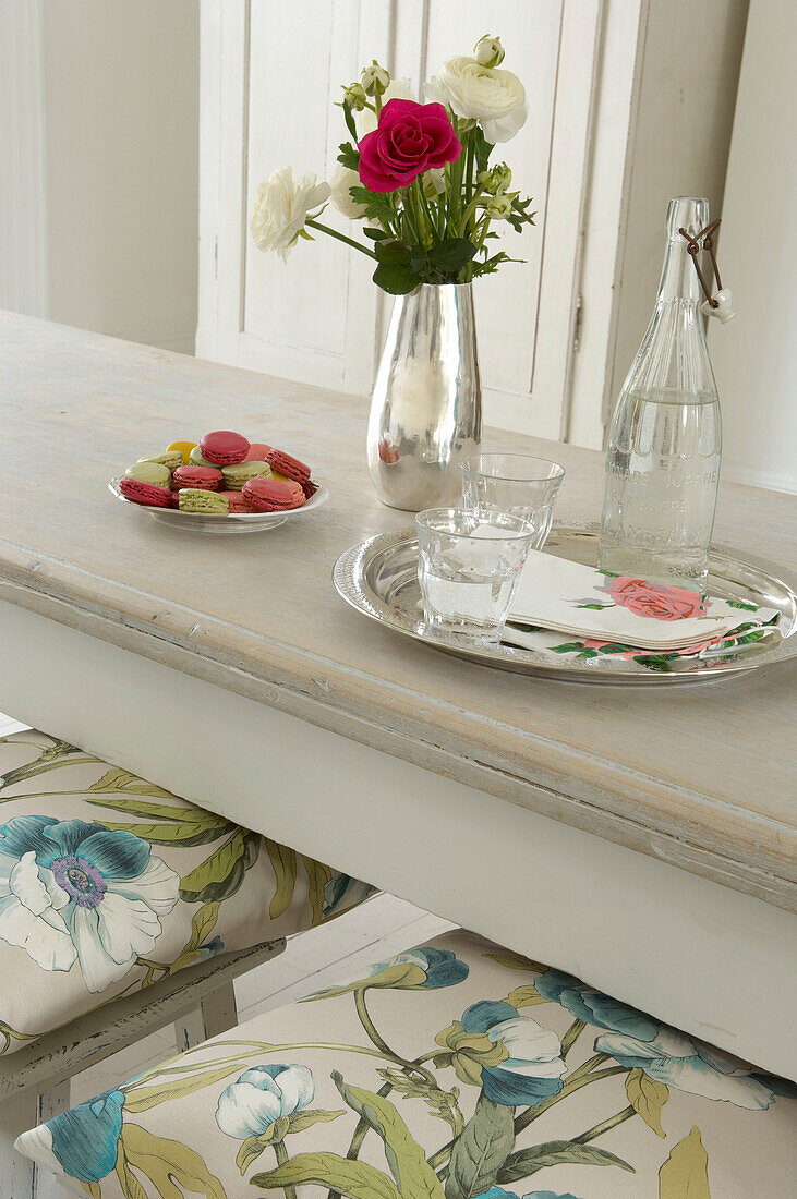 Vase of fresh flowers tray of drinks and biscuits on a white dining table