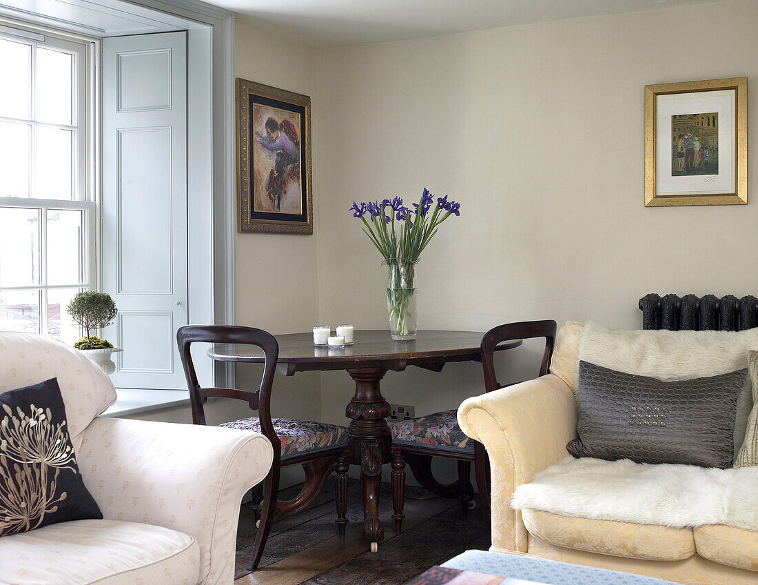 Dark wood dining table and sofas at shuttered window in Gloucestershire farmhouse, England, UK