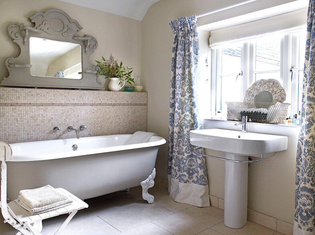 Freistehende Badewanne mit geblümten Vorhängen im Badezimmer eines Bauernhauses in Gloucestershire, England, UK