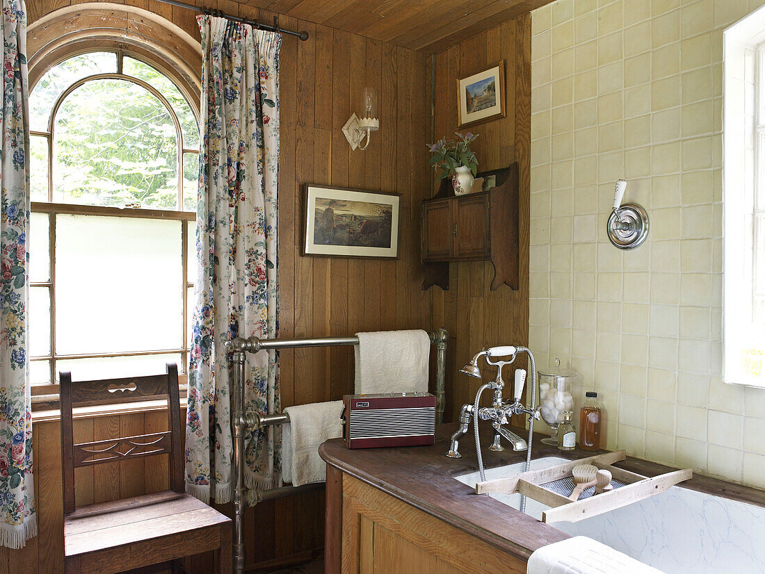 Gewölbtes Fenster mit geblümten Vorhängen im Badezimmer einer umgebauten Kapelle in Shropshire, England, UK