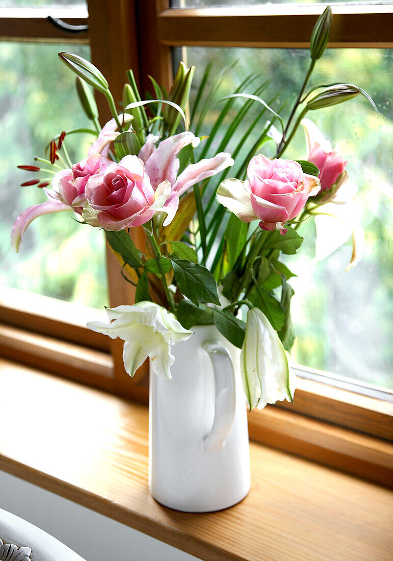 Krug mit Rosen und Lilien auf der Fensterbank eines Cottages in Gloucestershire, England, UK