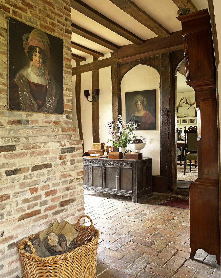 OIl paintings and grandfather clock in brick hallway of timber framed country house Suffolk, England, UK