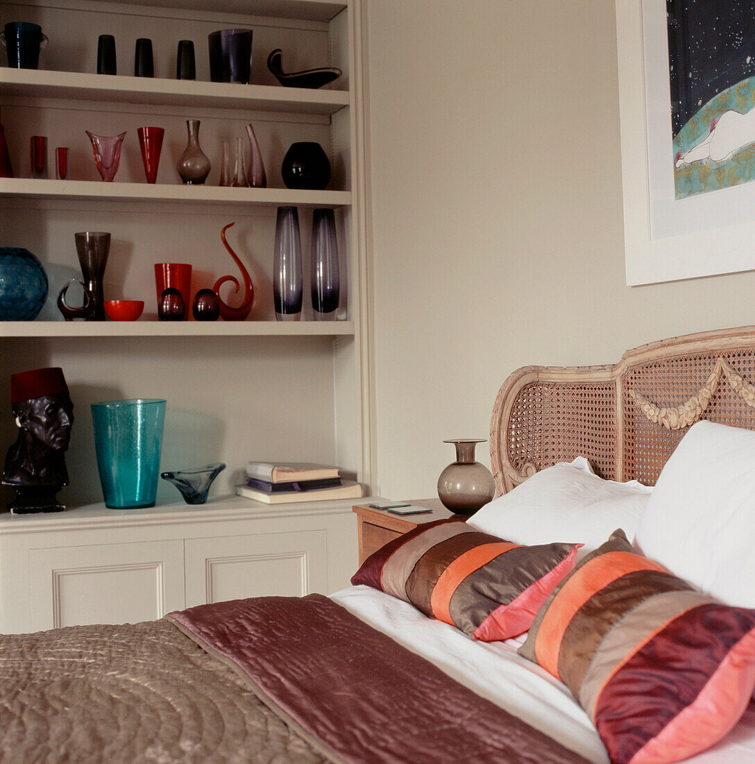 Schlafzimmer mit Doppelbett, offene Regale mit farbigen Vintage-Gläsern