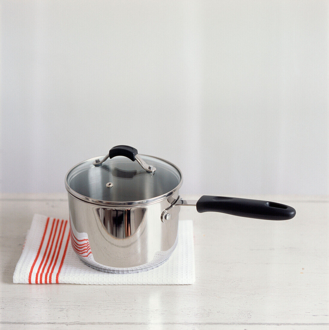 Metal saucepan resting on a tea towel on a white kitchen worktop