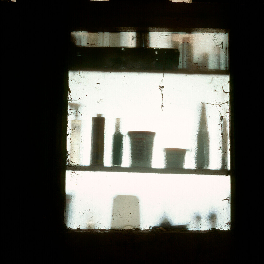 View of shed window with shadows of paint pots and DIY products on shelves