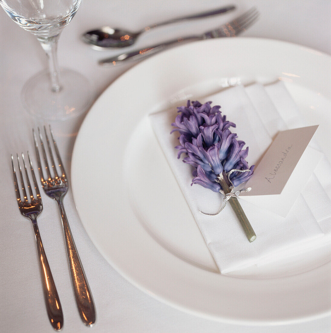 Detail of a white table setting with a name tag attached to a purple hyacinth