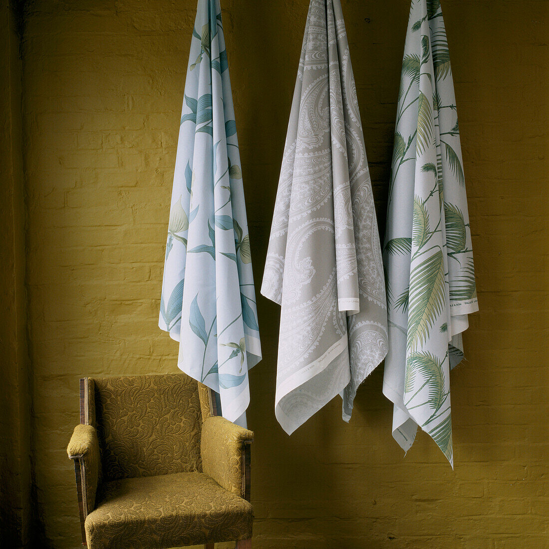 Fabric hanging on hooks against a painted brick wall and armchair 