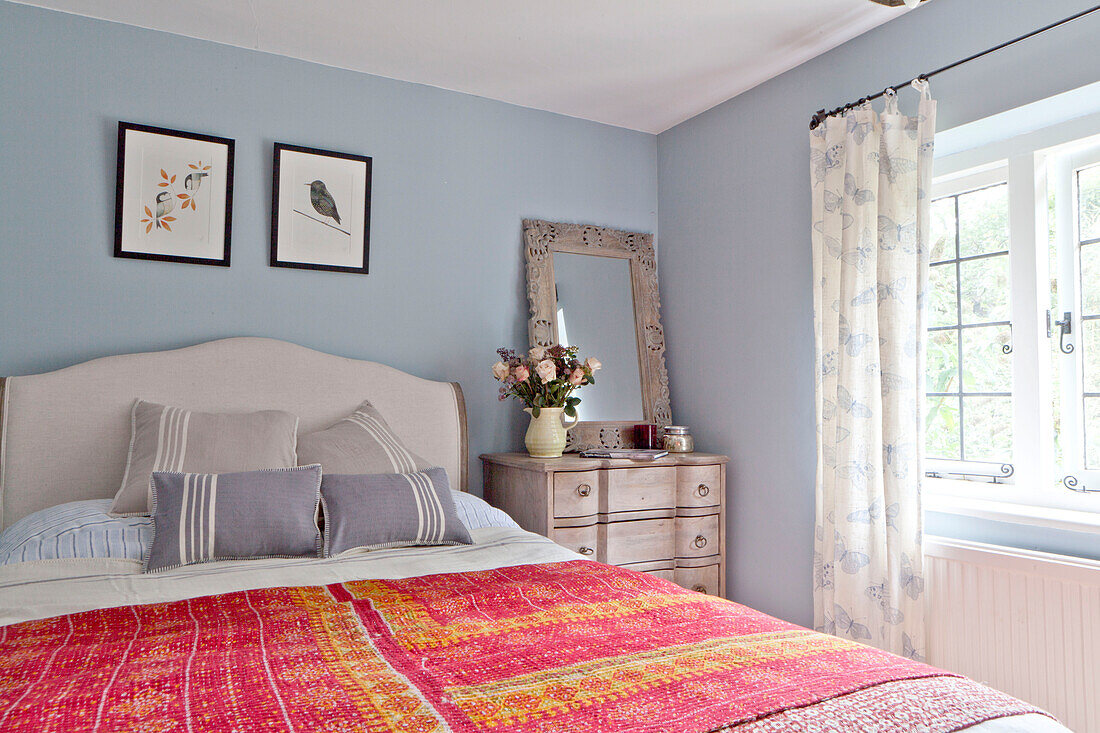 Red embroidered bed cover in blue bedroom of Surrey cottage England UK