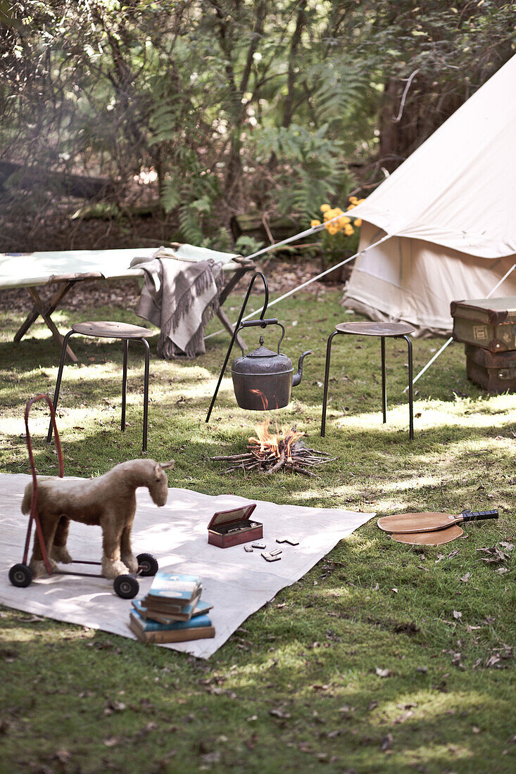 Pitched tent in garden with vintage toys and kettle on campfire, UK