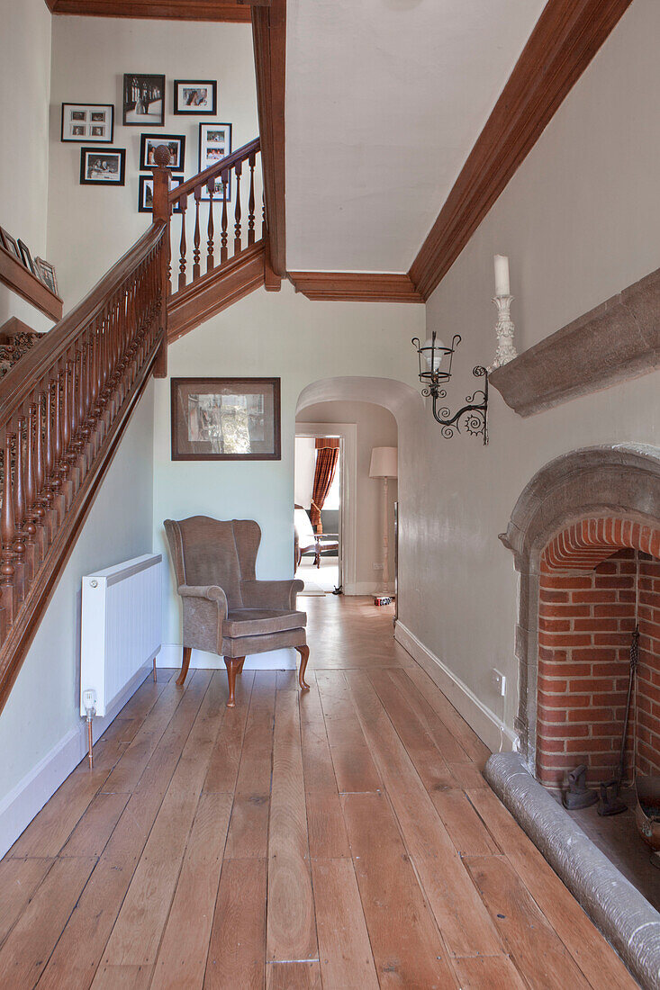 Exposed brick fireplace and wooden banister in hallway with wooden floorboards in Surrey home England UK