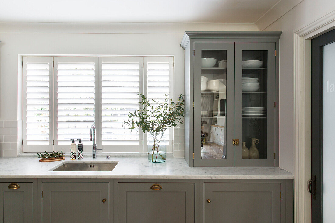 Glass fronted cabinet and leaf arrangement with closed shutters in London kitchen UK