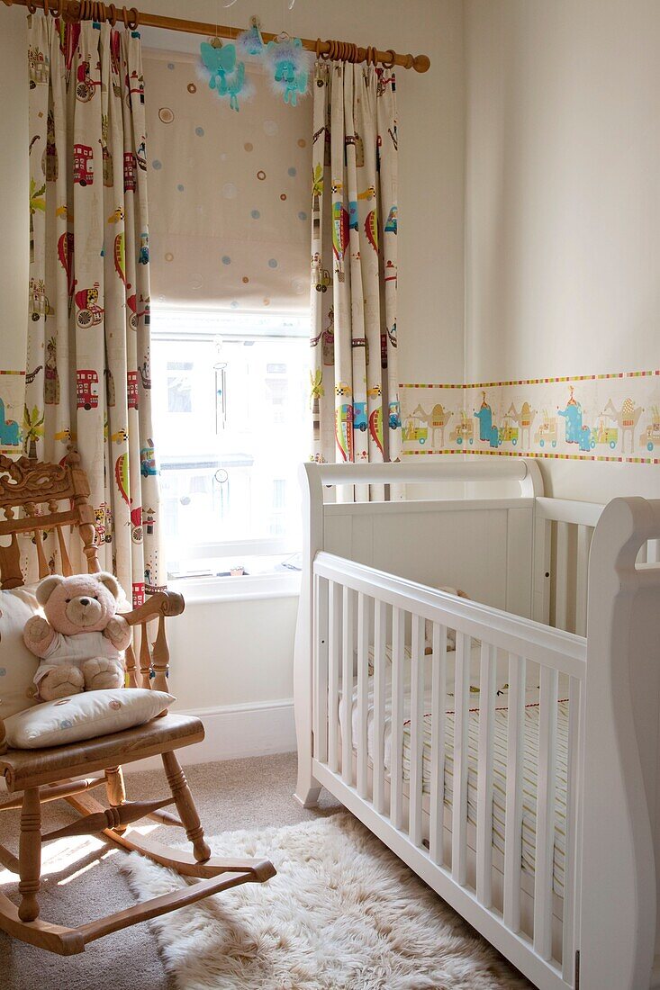 White painted crib with rocking chair at window in family home, UK