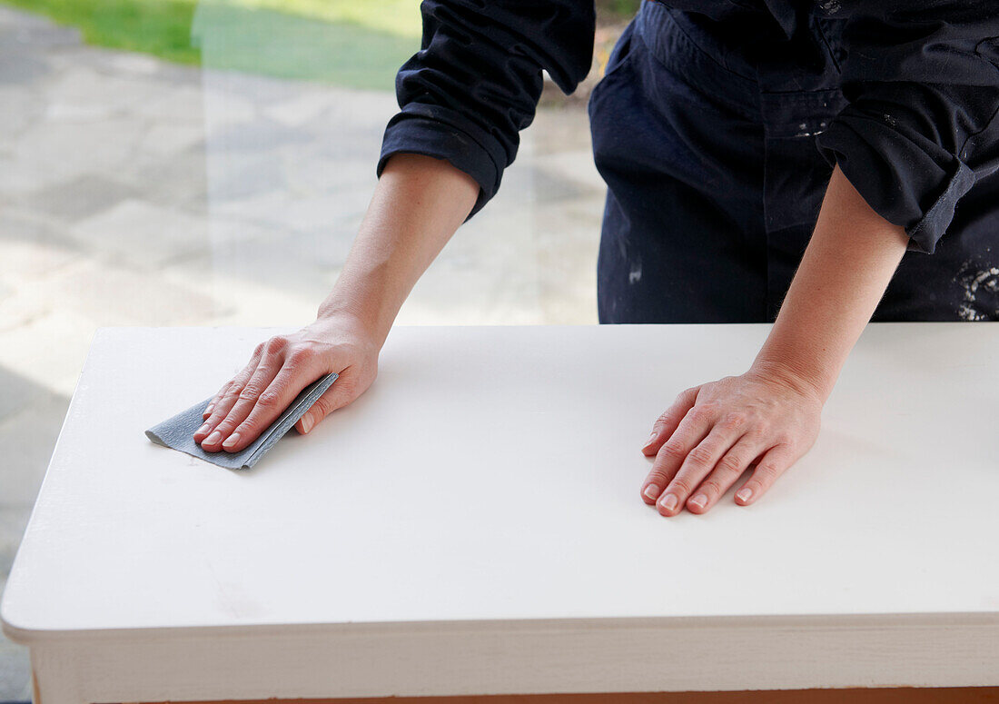 Woman in blue overalls sanding down sideboard in UK home