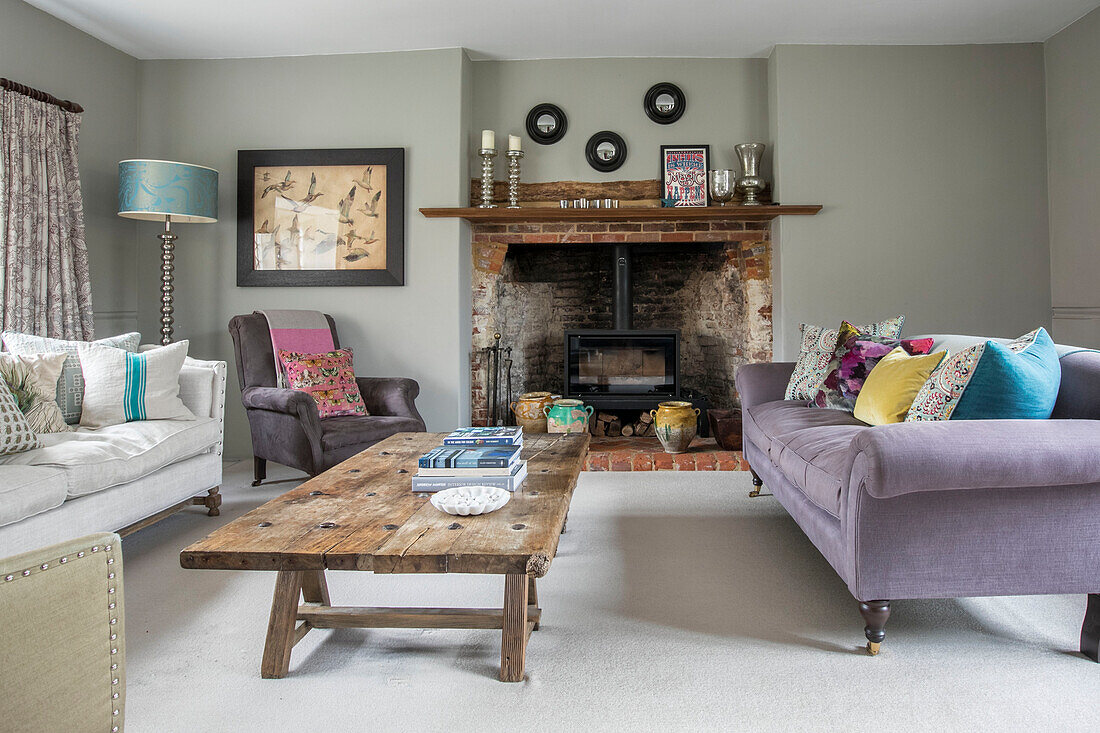 Lilac sofa and cushions at exposed brick fireside with low wooden coffee table in Grade II listed Jacobean house Alton UK