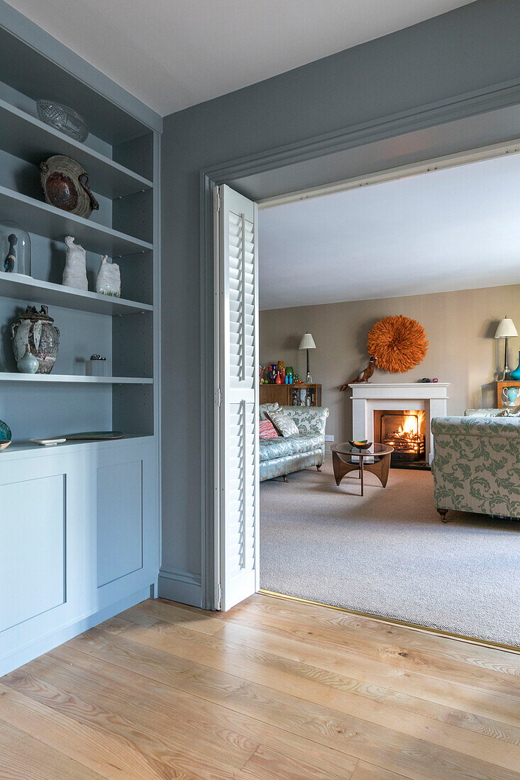 Hellblaues Regal mit Blick durch die Tür zum Wohnzimmer mit beleuchtetem Kamin in einem Haus in Farnham, Surrey, England